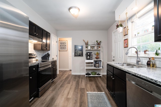 kitchen with decorative backsplash, appliances with stainless steel finishes, light stone countertops, sink, and hardwood / wood-style floors