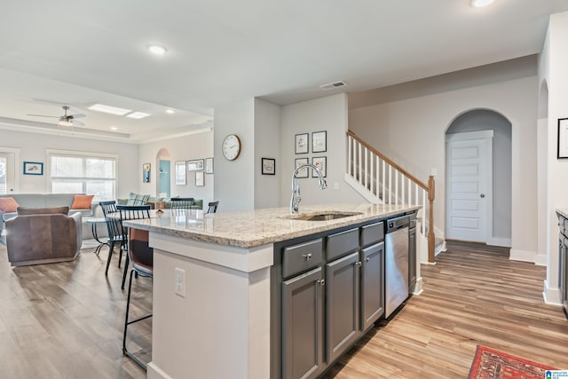 kitchen featuring stainless steel dishwasher, gray cabinetry, ceiling fan, a kitchen island with sink, and sink