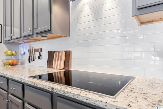 kitchen with gray cabinetry, decorative backsplash, light stone countertops, and black electric cooktop