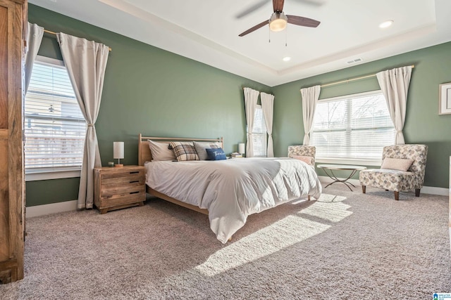 carpeted bedroom with ceiling fan and a tray ceiling