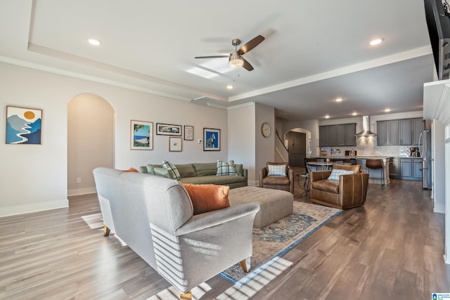 living room featuring a raised ceiling, ceiling fan, and light hardwood / wood-style flooring