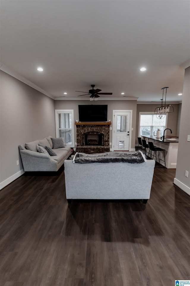 living room with dark wood-type flooring, sink, ceiling fan, ornamental molding, and a fireplace