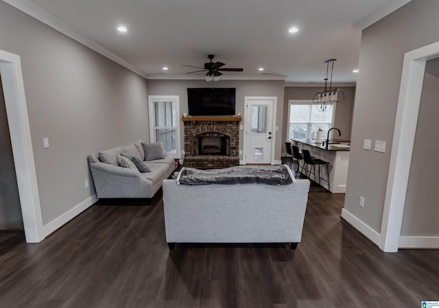 living room with ceiling fan, a fireplace, ornamental molding, and dark wood-type flooring