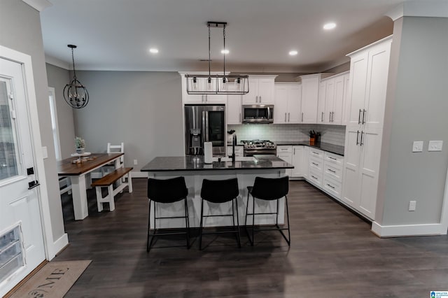 kitchen with white cabinets, decorative light fixtures, stainless steel appliances, and a kitchen island with sink