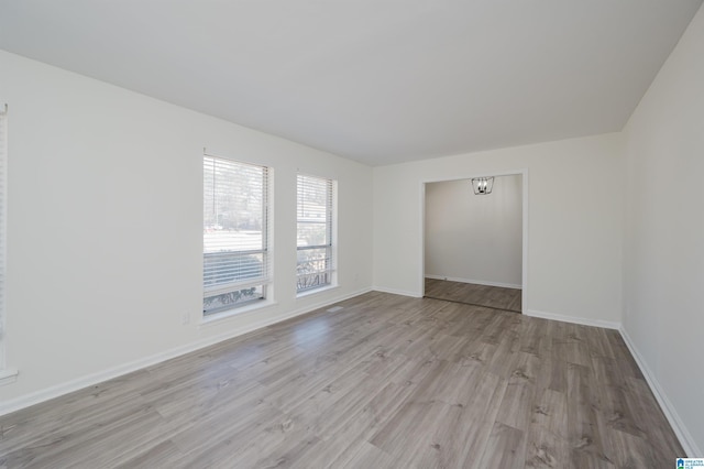 empty room featuring light wood-type flooring and a notable chandelier