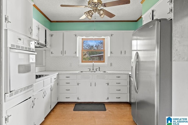 kitchen featuring oven, stainless steel fridge, white cabinetry, and sink