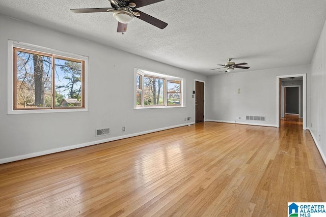 empty room featuring ceiling fan, a healthy amount of sunlight, a textured ceiling, and light wood-type flooring