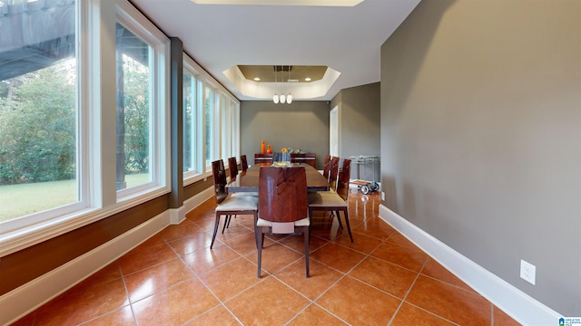 dining area with tile patterned flooring, a notable chandelier, and a raised ceiling