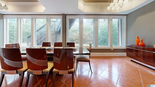 dining space with tile patterned flooring, a raised ceiling, ornamental molding, and an inviting chandelier