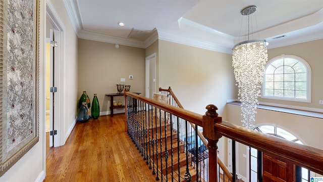 hall featuring a raised ceiling, ornamental molding, light wood-type flooring, and an inviting chandelier