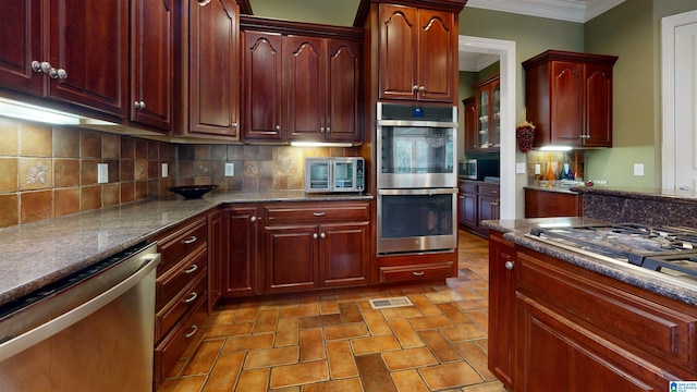 kitchen featuring decorative backsplash, dark stone countertops, ornamental molding, and appliances with stainless steel finishes