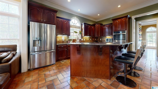 kitchen with a healthy amount of sunlight, backsplash, a kitchen island, a kitchen bar, and stainless steel appliances