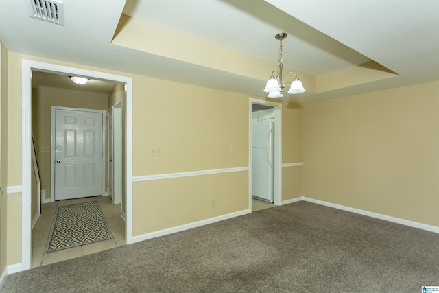 carpeted empty room with an inviting chandelier and a tray ceiling