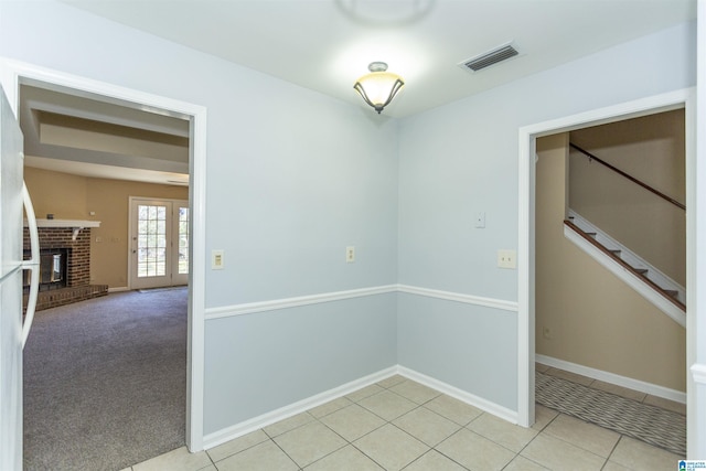 carpeted spare room with french doors and a brick fireplace