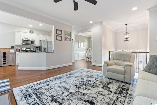 living room featuring ceiling fan with notable chandelier, dark hardwood / wood-style floors, crown molding, and sink