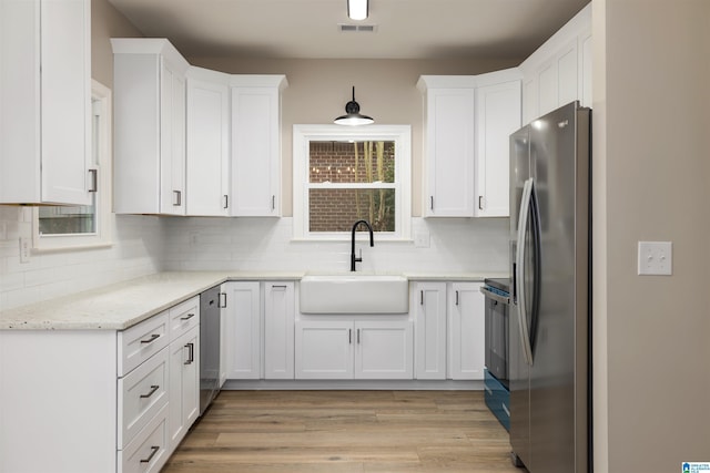 kitchen with light stone countertops, appliances with stainless steel finishes, tasteful backsplash, sink, and white cabinets