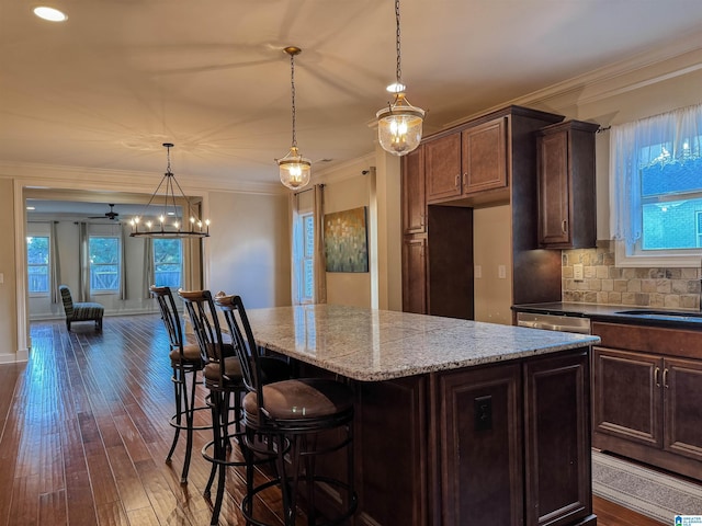 kitchen featuring ceiling fan, a kitchen island, light stone counters, and decorative light fixtures