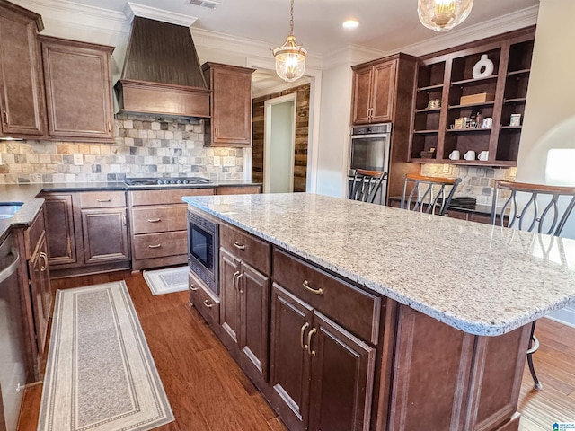 kitchen featuring dark hardwood / wood-style floors, pendant lighting, a breakfast bar area, custom exhaust hood, and appliances with stainless steel finishes