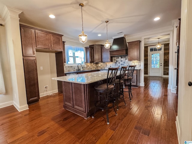 kitchen featuring decorative backsplash, premium range hood, light stone counters, decorative light fixtures, and a kitchen island