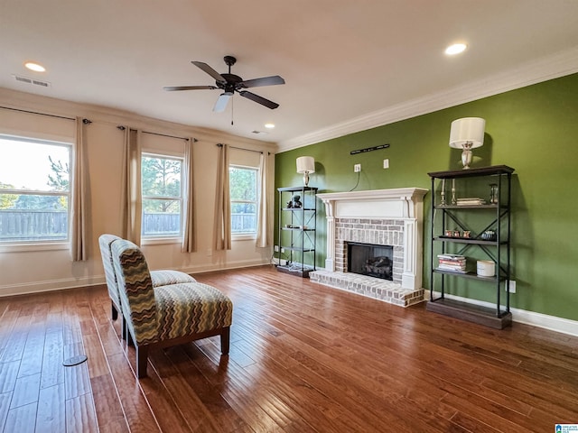 living area with ceiling fan, wood-type flooring, ornamental molding, and a brick fireplace