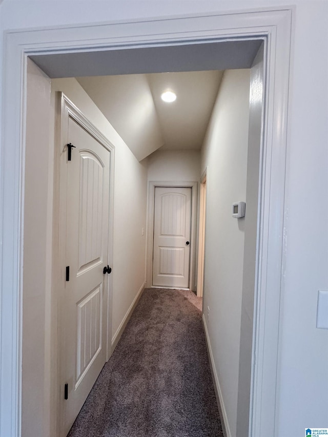 hallway with dark carpet and vaulted ceiling