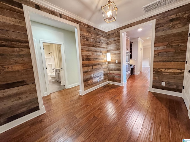 spare room featuring hardwood / wood-style floors, ornamental molding, a notable chandelier, and wood walls