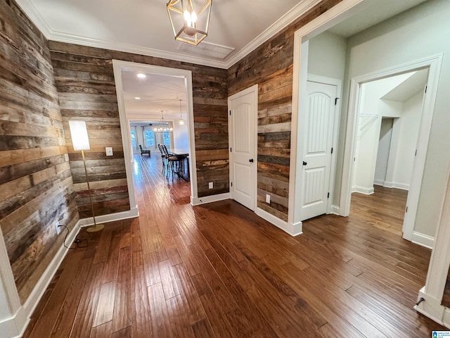 hallway with wooden walls, hardwood / wood-style floors, ornamental molding, and an inviting chandelier