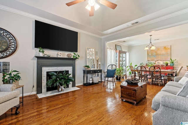 living room featuring a fireplace, ceiling fan with notable chandelier, hardwood / wood-style flooring, and crown molding