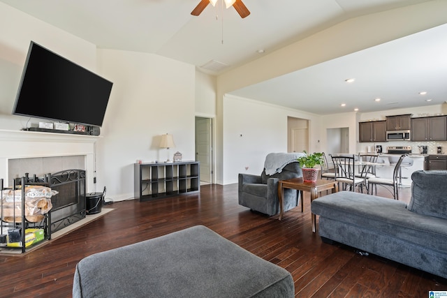 living room with a fireplace, vaulted ceiling, ceiling fan, and dark wood-type flooring