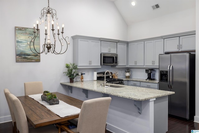 kitchen featuring hanging light fixtures, light stone countertops, appliances with stainless steel finishes, a kitchen bar, and kitchen peninsula