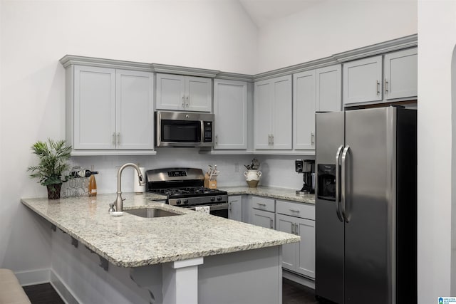 kitchen with light stone counters, kitchen peninsula, gray cabinets, decorative backsplash, and appliances with stainless steel finishes