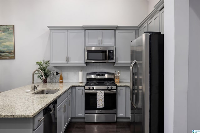 kitchen featuring kitchen peninsula, appliances with stainless steel finishes, backsplash, light stone countertops, and sink