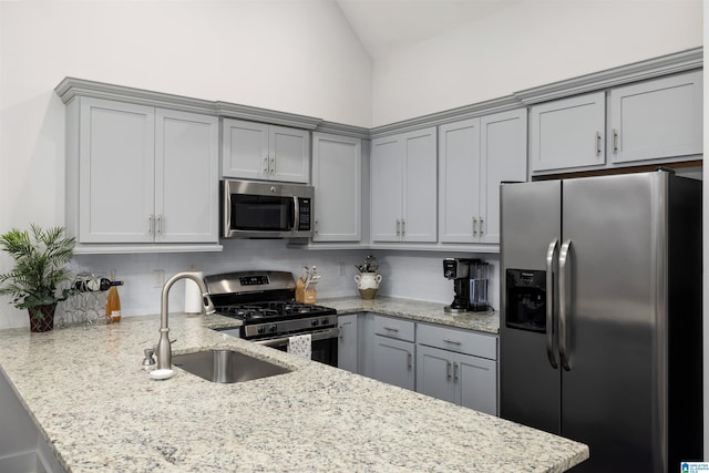 kitchen with backsplash, sink, light stone countertops, appliances with stainless steel finishes, and kitchen peninsula