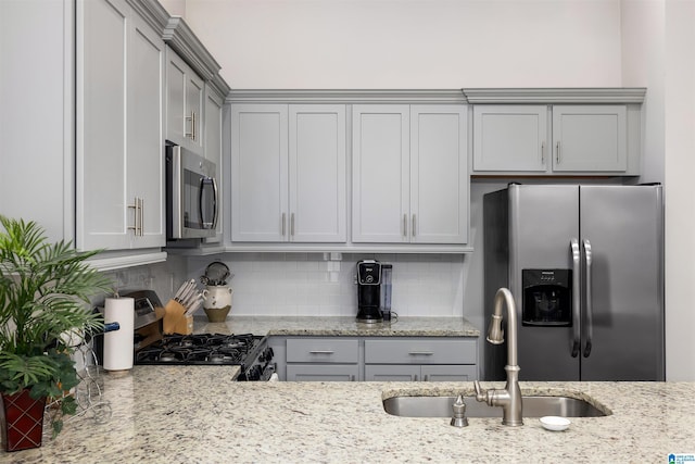 kitchen with gray cabinetry, sink, stainless steel appliances, tasteful backsplash, and light stone counters