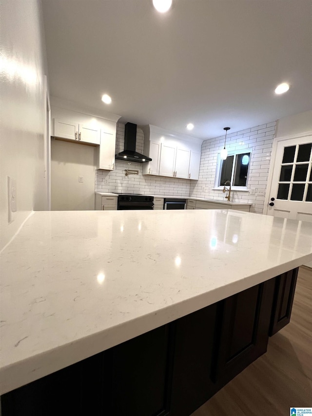 kitchen with light stone countertops, wall chimney exhaust hood, dark hardwood / wood-style flooring, oven, and white cabinets