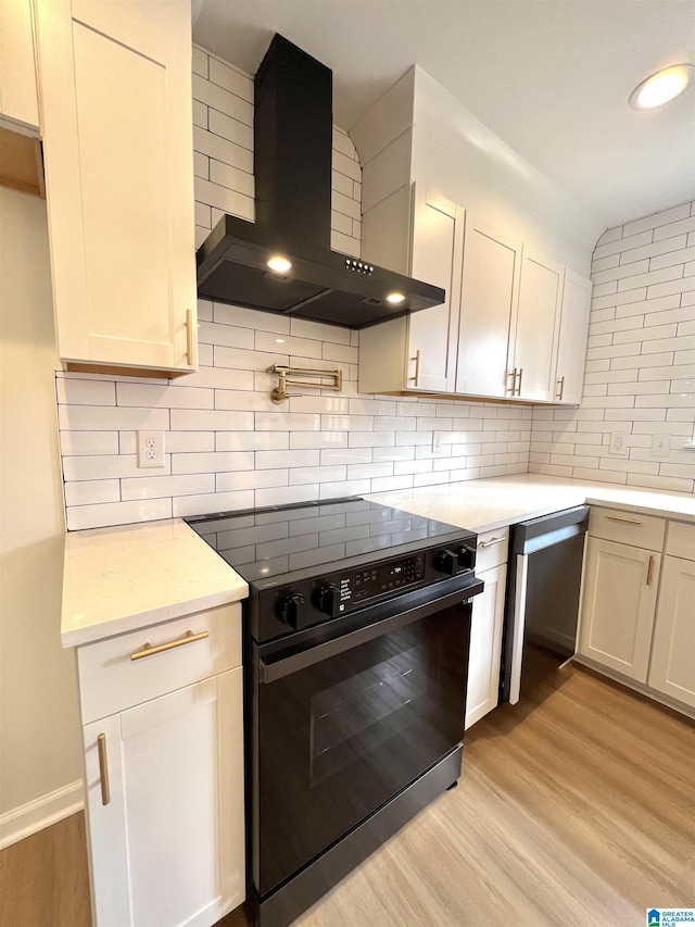 kitchen featuring black electric range oven, wall chimney range hood, and white cabinetry