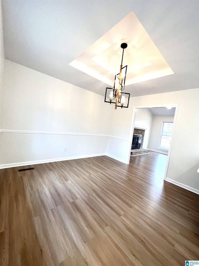 unfurnished living room featuring a raised ceiling, hardwood / wood-style flooring, a fireplace, and an inviting chandelier