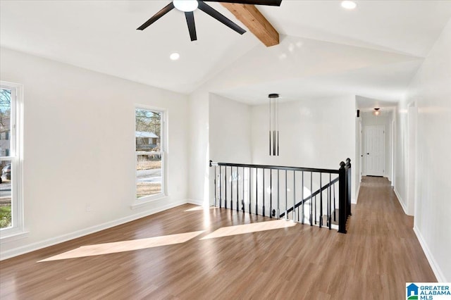 empty room with lofted ceiling with beams, light hardwood / wood-style flooring, ceiling fan, and a healthy amount of sunlight