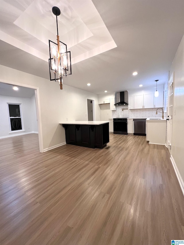 kitchen featuring wall chimney exhaust hood, a raised ceiling, dishwasher, white cabinetry, and hanging light fixtures