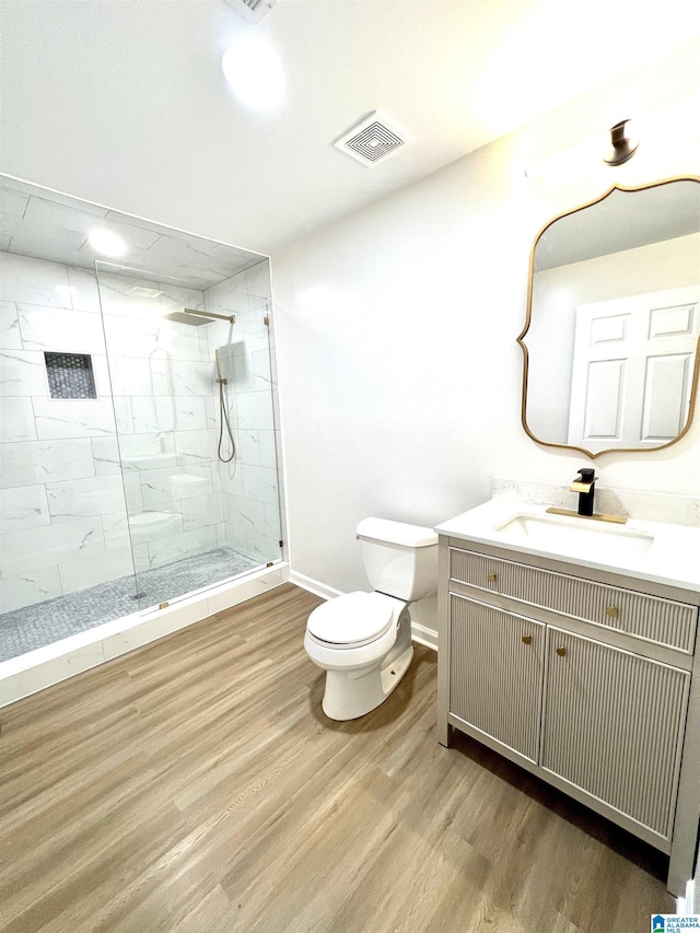 bathroom with a tile shower, hardwood / wood-style floors, vanity, and toilet