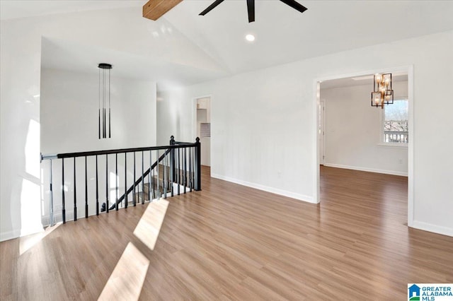 empty room with hardwood / wood-style floors, lofted ceiling with beams, and ceiling fan with notable chandelier