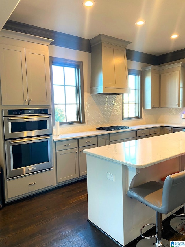 kitchen with gray cabinetry, a breakfast bar, premium range hood, light stone countertops, and stainless steel appliances