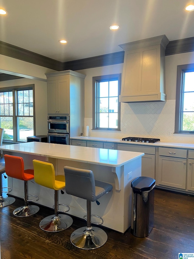 kitchen with dark wood-type flooring, appliances with stainless steel finishes, a kitchen island, custom range hood, and a breakfast bar area