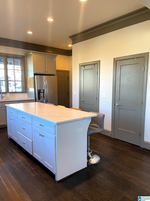 kitchen featuring white cabinets, light stone countertops, a kitchen island, dark hardwood / wood-style flooring, and stainless steel fridge with ice dispenser