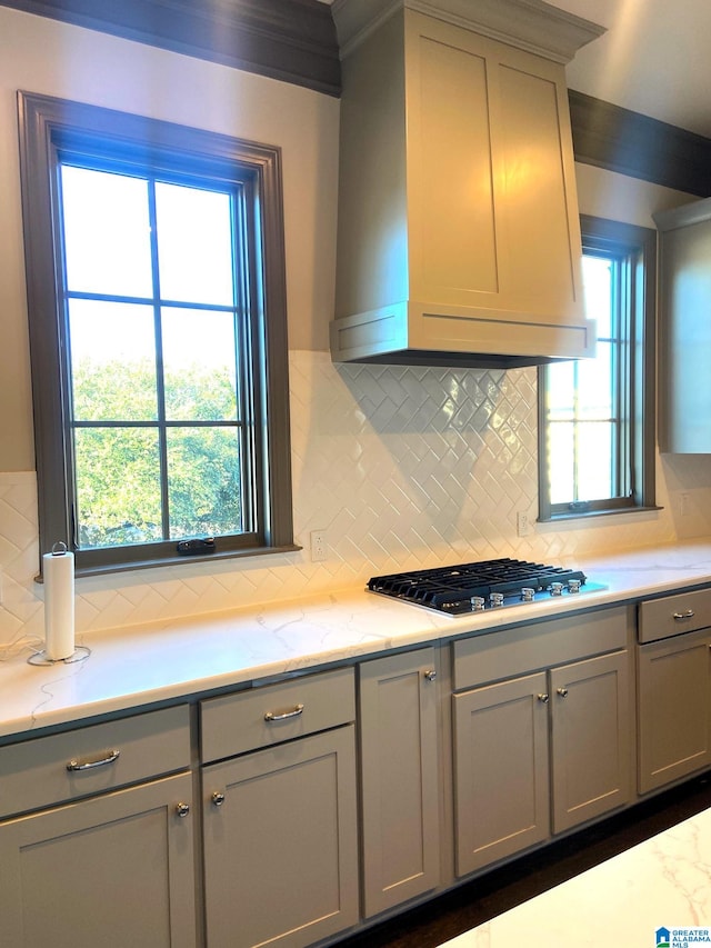 kitchen featuring gray cabinetry, wall chimney exhaust hood, decorative backsplash, light stone countertops, and gas cooktop