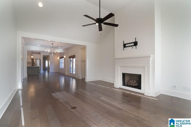 unfurnished living room with lofted ceiling, crown molding, dark wood-type flooring, and ceiling fan with notable chandelier