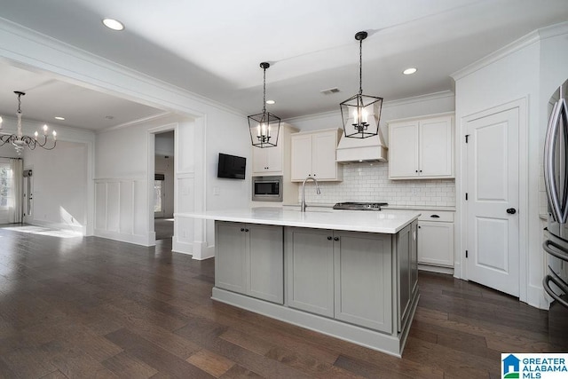 kitchen featuring decorative light fixtures, a center island with sink, white cabinetry, and stainless steel microwave