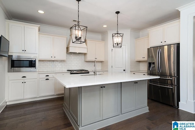 kitchen with a center island with sink, white cabinets, hanging light fixtures, and appliances with stainless steel finishes