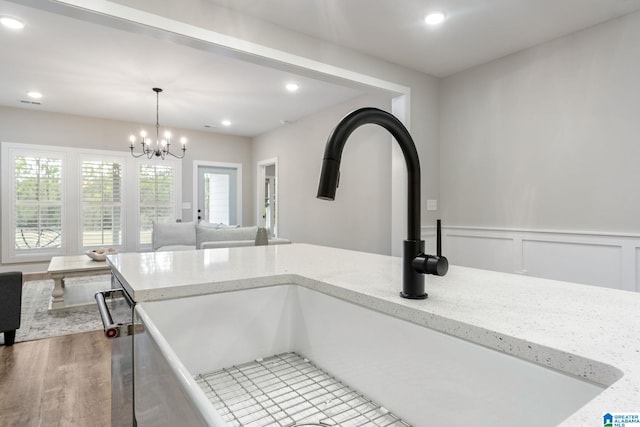 kitchen with a chandelier, decorative light fixtures, light stone counters, and sink