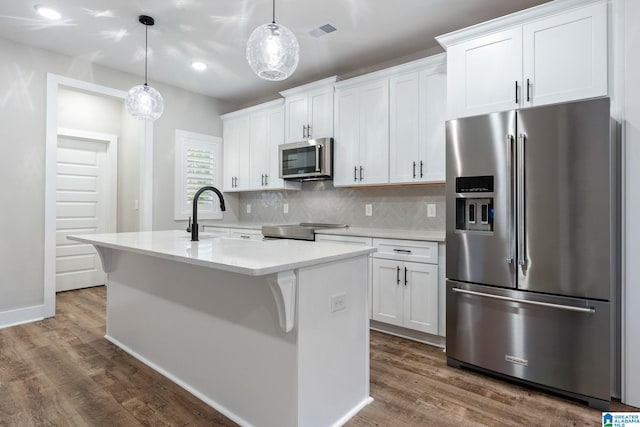 kitchen with white cabinets, appliances with stainless steel finishes, hanging light fixtures, and an island with sink